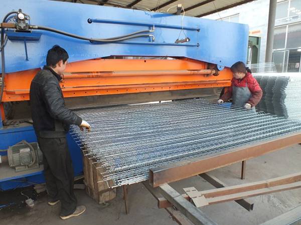 A bending machine is bending the welded wire mesh panels and two worker are working beside it.