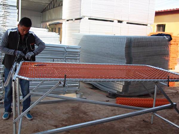A worker is wrapping the chain link mesh onto frame with steel wires.