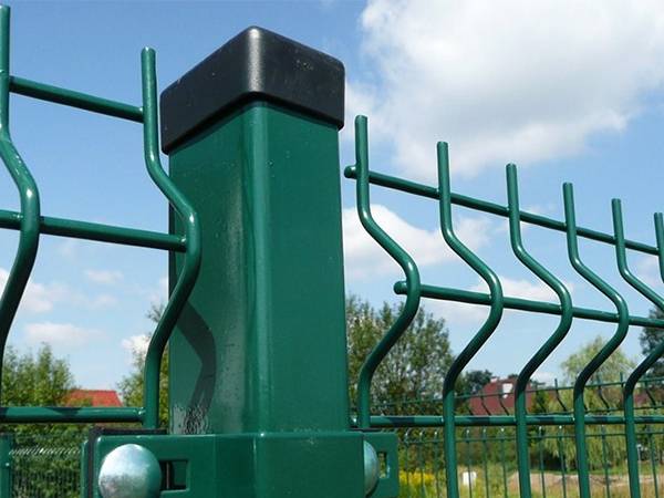 Curvy wire mesh fences are connected with a square post by green clips.