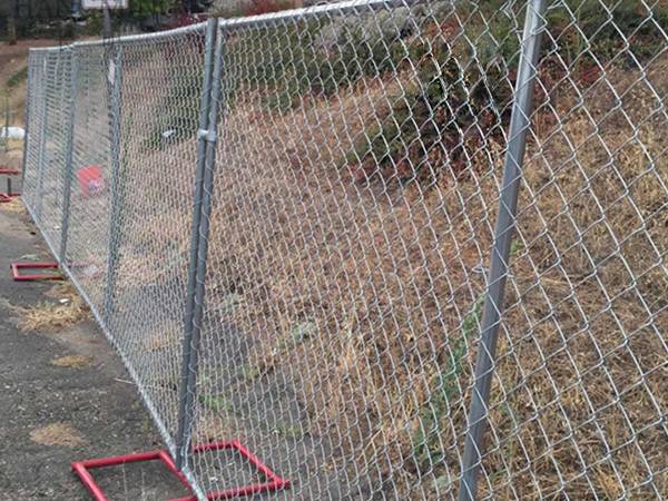 Temporary chain link fence with red square tubular fence feet installed by the roadside.