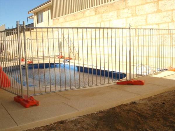 Temporary pool fencing with orange plastic feet in the backyard surrounding swimming pool.